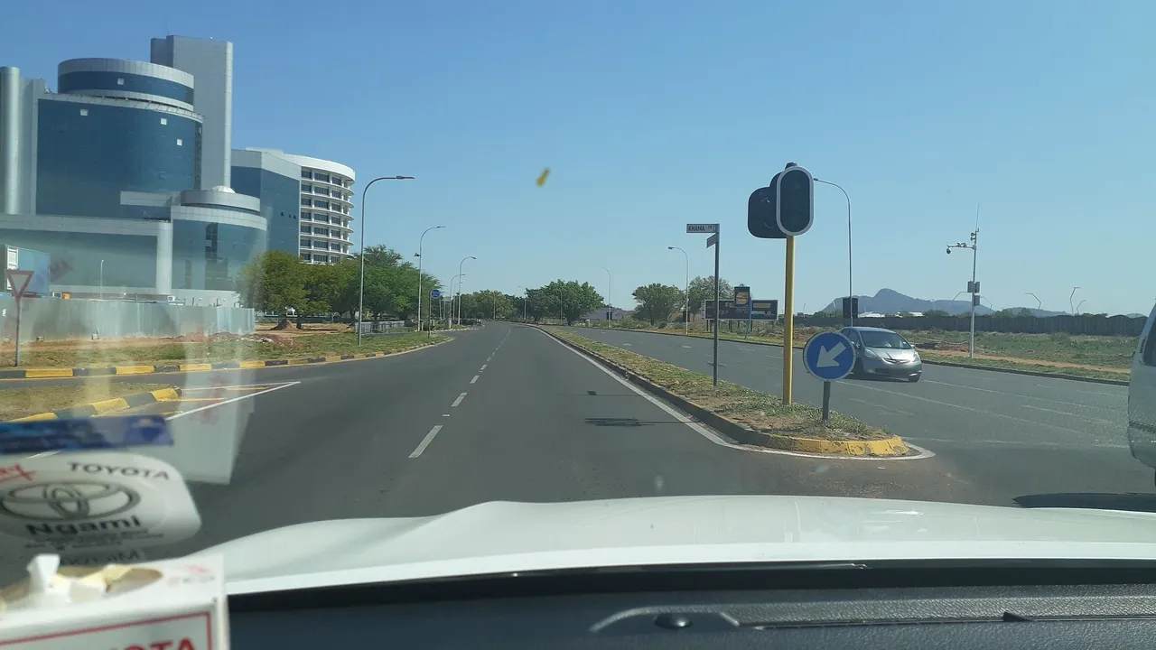 A keep-left sign, yellow-and-black median, and dry urban trees on a broad road.