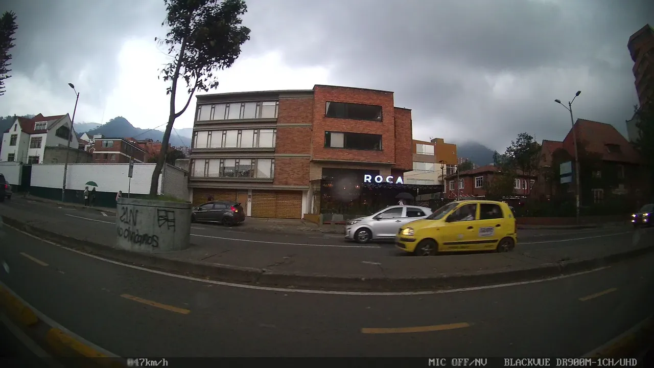 A yellow taxi, a brick-faced building, and mountains visible behind the street.