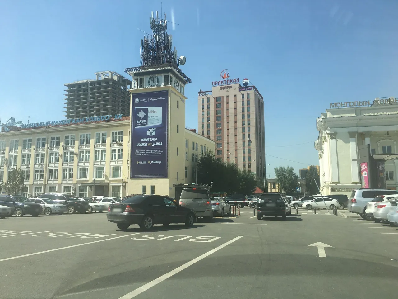 Cyrillic rooftop signs including МОНГОЛЫН, a broad road and a dry urban setting.
